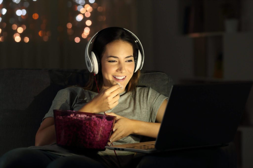women eating popcorn watching a computer with headphones